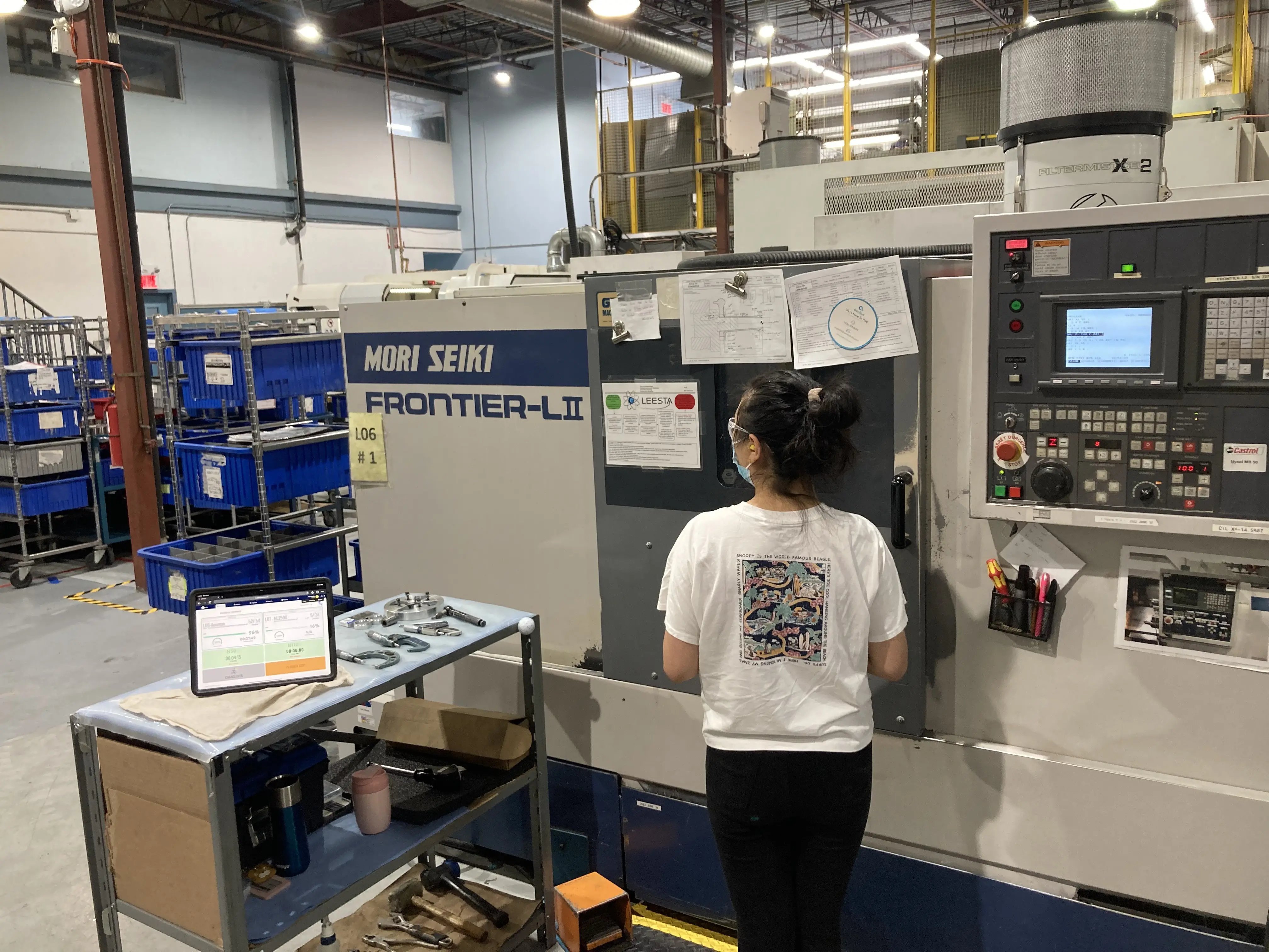 CNC machinist in front of a machine looking at JITbase on a tablet