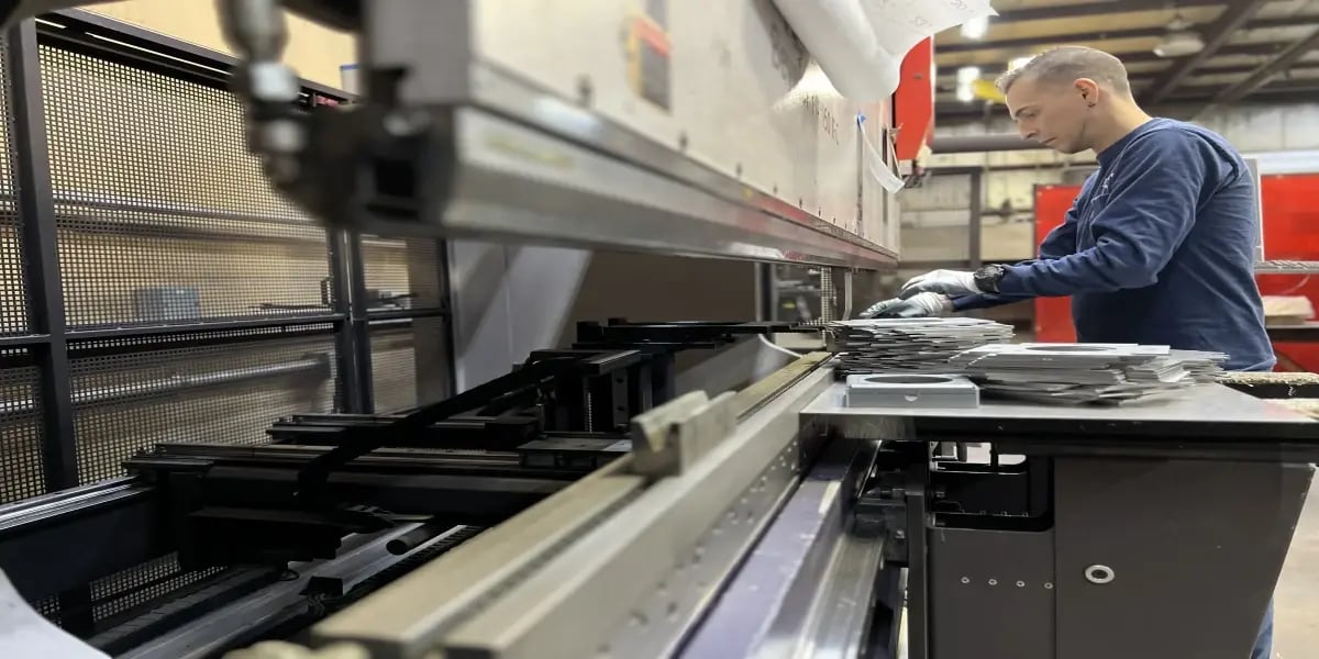 Operator working at a press brake with stacked metal parts, illustrating production waiting for quality inspection — JITbase.