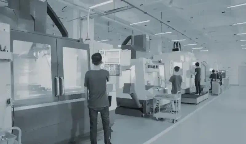 Manufacturing workshop with multiple CNC machines, each operated by a technician, illustrating the one-operator-per-machine production model.